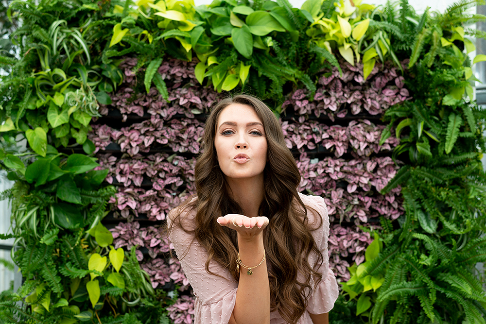 Woman blowing a kiss in front of greenery